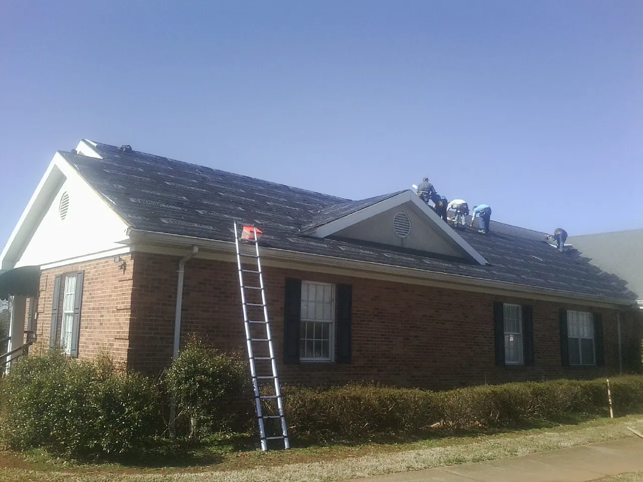 Crew tearing shingles off a brick ranch roof with a ladder set — Metal Roof Repair work by our crew in Beverly