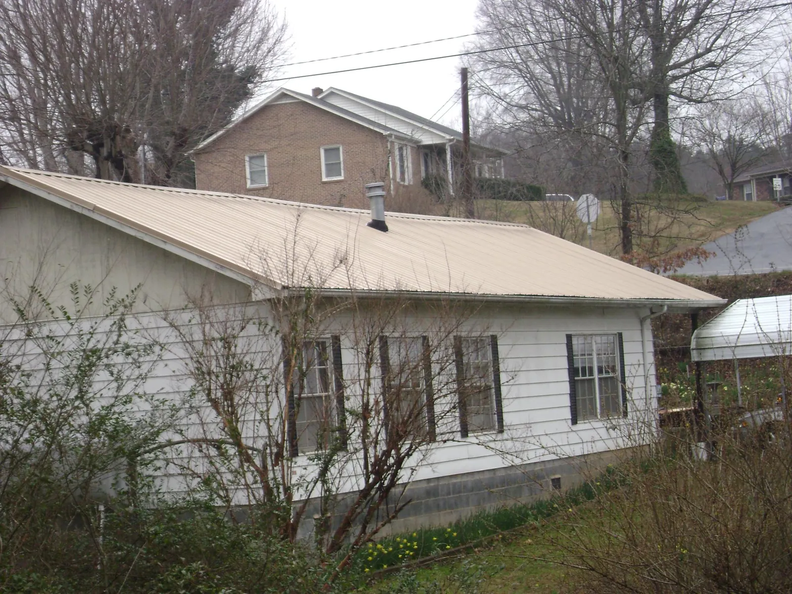Tan metal roof on a white sided house set into a hillside — Commercial Roofing by Roofing Brothers in Beverly